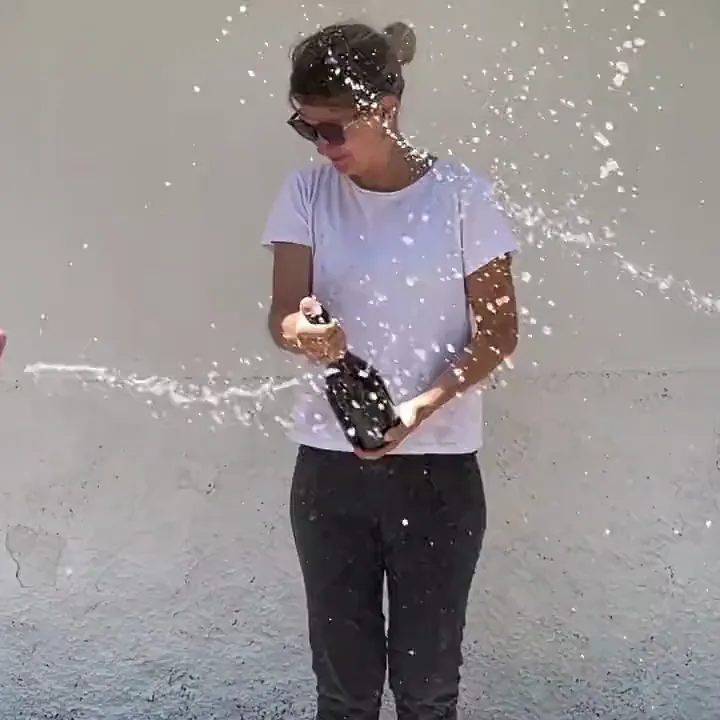 Celebration bottles are opened and water sprays across a woman holding one